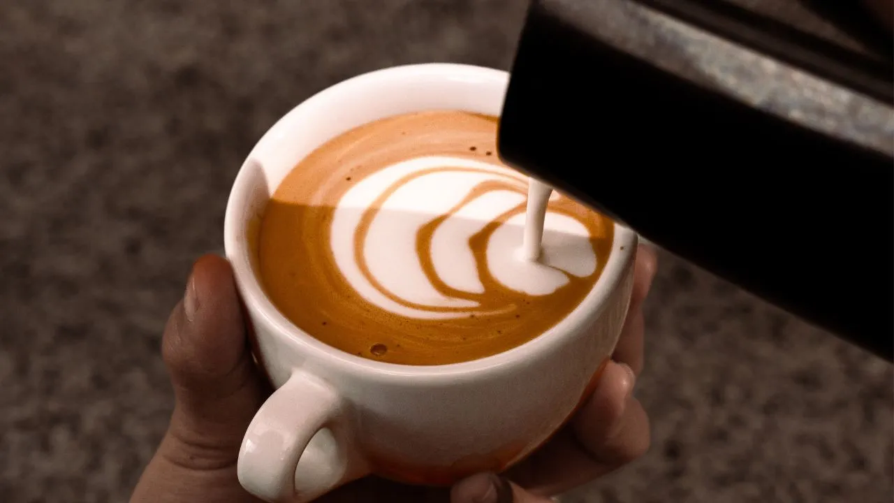 Barista pouring milk into espresso to create latte art, showcasing consistency in coffee preparation